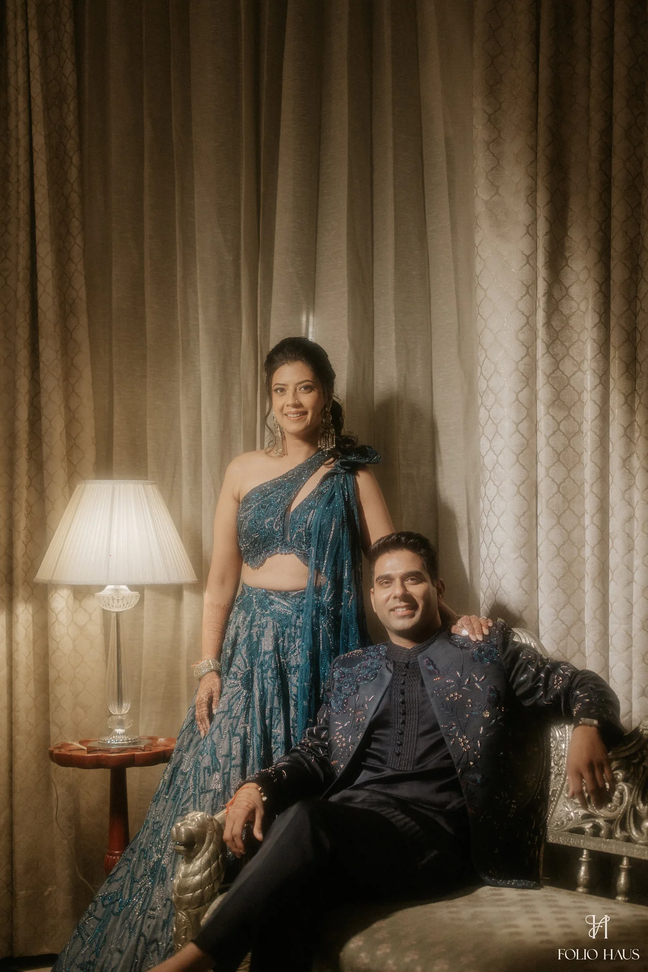 Jigna standing beside Anurag seated in a warmly lit room.