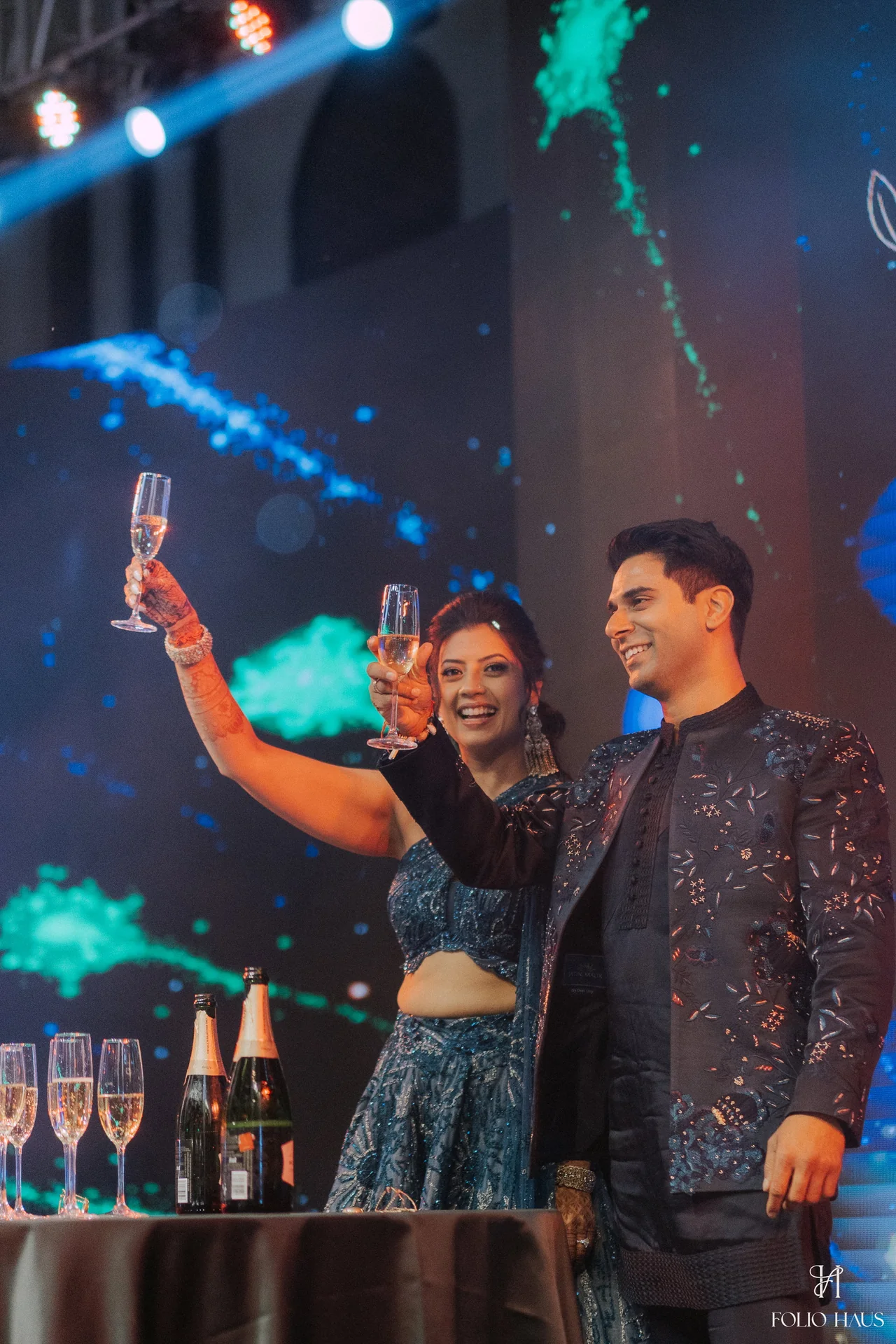 Jigna and Anurag celebrating on stage with raised glasses.