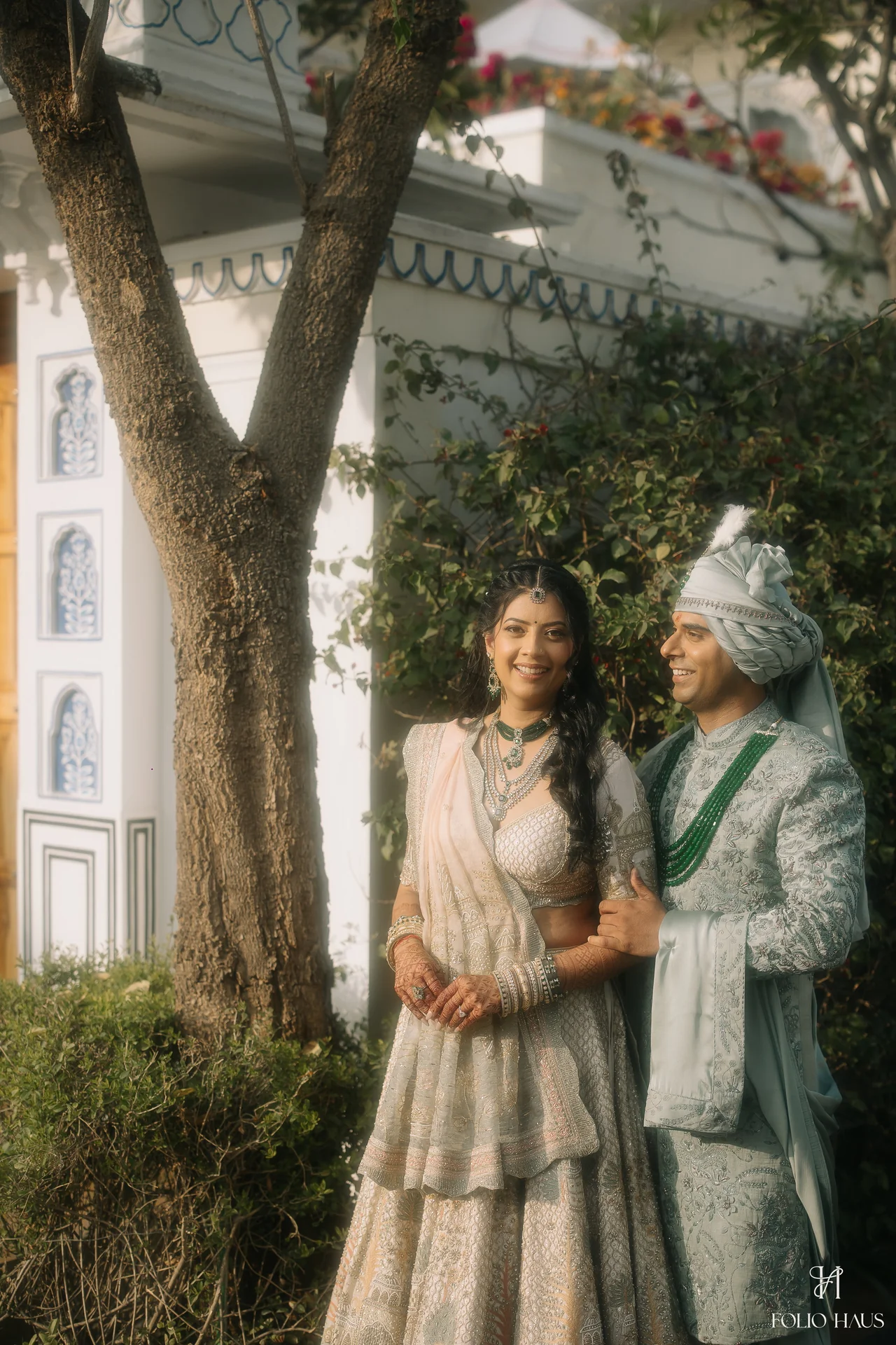 Jigna and Anurag standing together beneath trees beside the palace.